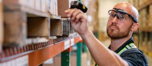 An employee wearing smart glasses while inspecting stock on warehouse shelves.